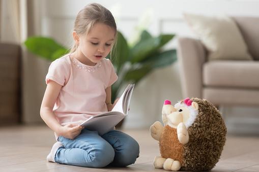 Petit hérisson en peluche à côté d'une fillette lui lisant un livre